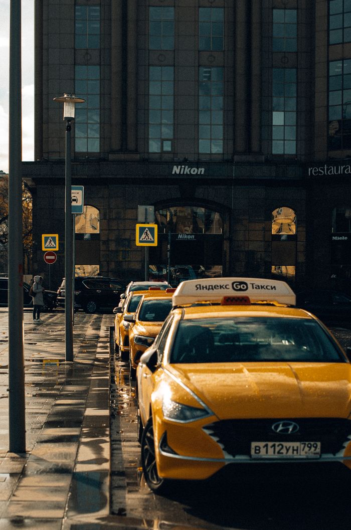 contact-img Urban scene featuring parked yellow taxis on a city street in front of a building on a rainy day.