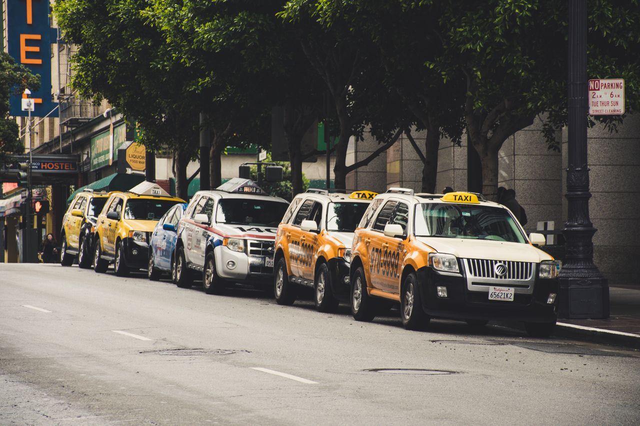 services-img A row of taxis parked on a city street with trees and urban background.