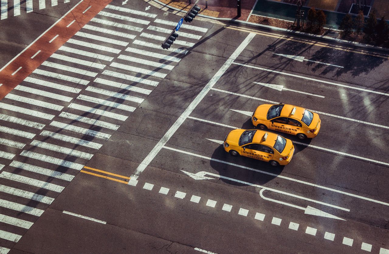 services-04 Two yellow taxis navigate a city intersection with marked pedestrian crossings.