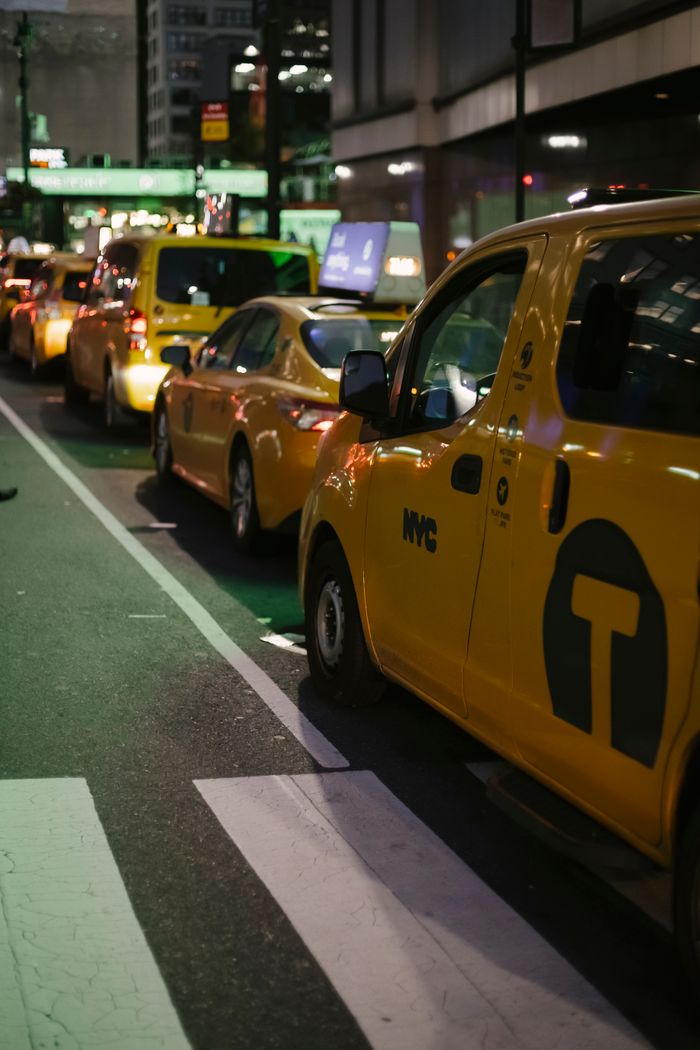 Row of modern various yellow taxi vehicles parked on city street near buildings in New York at night